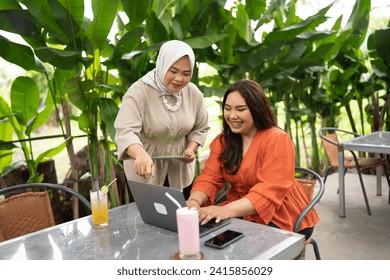 muslim woman metoring her coworker in an outdoor cafe with pointing at laptop hand gesture - Powered by Shutterstock