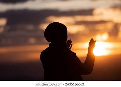 Muslim woman prayer praying with hands up open doing dua at sunset worship Allah. - Powered by Shutterstock