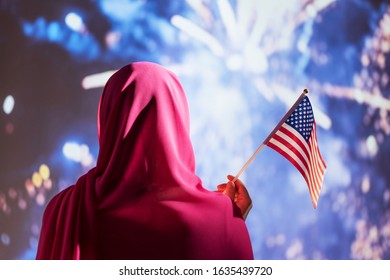 Muslim woman in a scarf holding American flag  during fireworks at night.  - Powered by Shutterstock