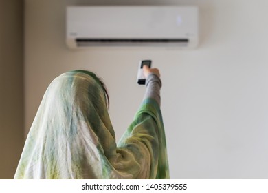 Muslim woman in a scarf  holding remote controller from air conditioner inside the room. 