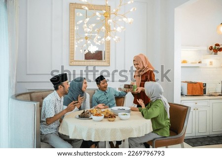 muslim woman serving drink for her friend and family at home having dinner together