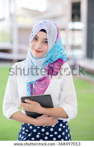 Muslim woman standing , holding tablet computer