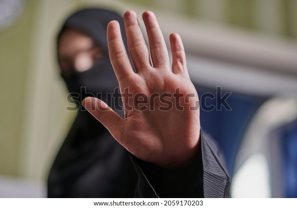 A Muslim woman in traditional black clothing nikab\
showing stop hand gesture. Role of women in Islamic world. Domestic\
violence, discrimination of Muslim women. Stop domestic violence\
against women
