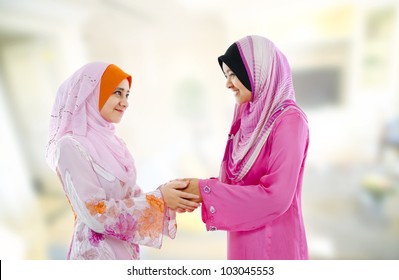 Muslim woman in traditional clothing greeting to each other, indoor.