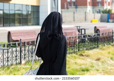 A Muslim woman walking down a city street in a black national outfit, a view from the back.