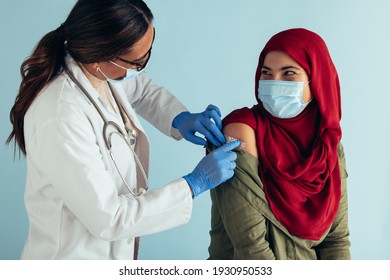 Muslim Woman Wearing Face Mask Getting Covid-19 Vaccine Shot From A Female Doctor. Healthcare Professional Putting Band-aid On Arm Of A Woman After Giving Her Vaccine.