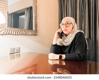 A Muslim woman wearing a hijab focuses on listening to a phone call from a client or friend regarding a work project. - Powered by Shutterstock