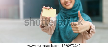 Muslim woman wearing hijab holding credit card with thumbs up gesture.