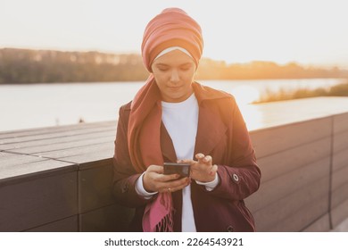 Muslim woman wearing hijab using mobile phone outdoor. Arabic woman wearing headscarf using smartphone on street. Islamic girl texting a message phone in city centre. - Powered by Shutterstock