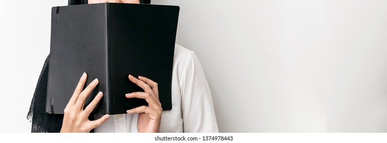 Muslim Woman Wearing Hijab, White Shirt And Holding A Black Cover Book In Front Of Her With Copy Space.