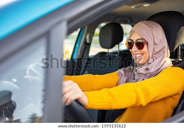 Muslim Woman wearing light hijab in a car\
lifestyle shoot. Beautiful muslim woman with toothy smile driving\
car. Portrait of a Middle Eastern woman driving a car, she is\
wearing a modern beige\
Abaya.