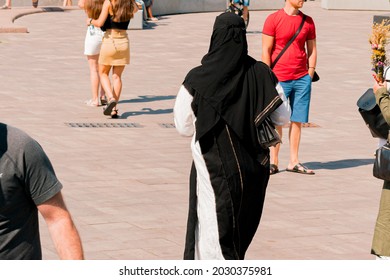 Muslim Woman Wearing White And Black Clothes Going Through The Noisy Street. City. Urban. Outdoor. Pedestrians. Sidewalk. Pathway. Public