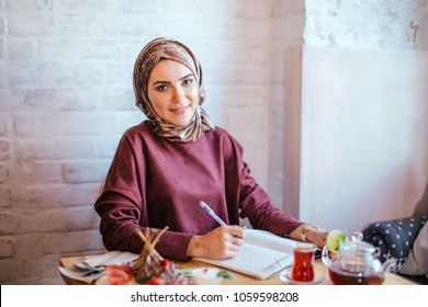 Muslim Woman Working In Cafe, Writing On Notepad