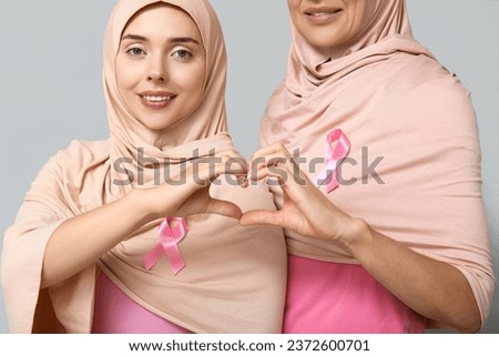 Muslim women with pink ribbons making heart with hands on grey background. Breast cancer awareness concept