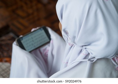 A Muslim Women In Praying Attire Reading Quran From Her Mobile Phone. DOF. Low Light By Intention.