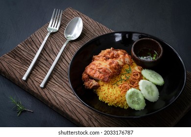 Muslim yellow rice with fried chicken in a black plate with little bowl seasoning on the old wooden plank above the dark kitchen table, halal food top view, Asian food or Thai food cuisine menu - Powered by Shutterstock