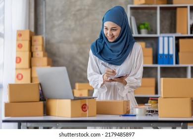 Muslim Young Asian Woman Working At Home Doing Sme Ecommerce Online Small Business Entrepreneur Checking Postal Parcels To Delivery To Online Customers, Startup Muslim Sme Business Concept.