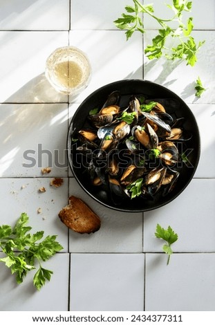 Mussels cooked and served with dry white wine and baguette, high angle view of ready to eat dish standing on a simple vintage tile kitchen surface