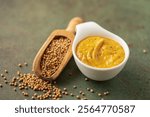 Mustard sauce in a bowl and seeds on a green background.