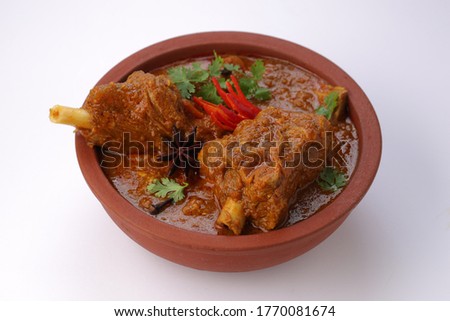 Mutton curry or Lamb curry,spicy and delicious dish garnished with coriander leaf ,red chilli  and star anise  spice in an earthenware bowl with white background.