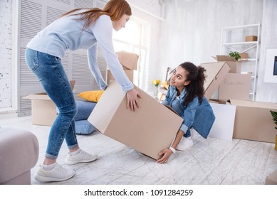 Mutual Assistance. Kind Young Girl Helping Her Roommate To Lift Up A Heavy Box While Packing Their Belongings Before Moving Out Of The Shared Flat