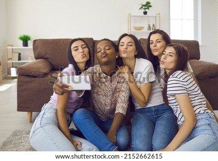 Mwah. Girls take group selfie to keep good memories and capture funny moment with friends. Happy diverse young women holding mobile phone, looking at screen, saying muah and making kissing duck face