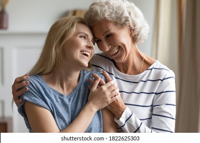 My beloved god-child. Tender caring elegant old lady god-mother embracing shoulders of grown up god-daughter, mature silver mom and adult kid girl standing close, touching foreheads and smiling - Shutterstock ID 1822625303
