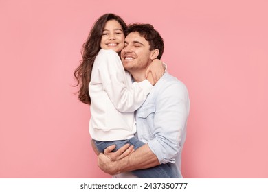 My best daddy. Happy daughter embracing her father as man holds girl in arms, both smiling, posing over pink studio backdrop - Powered by Shutterstock