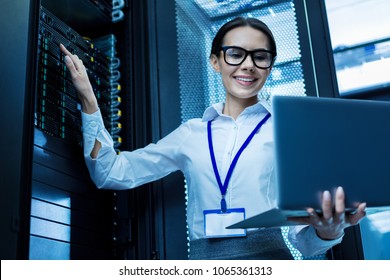 My best day. Content attractive woman working in a server cabinet and holding her laptop