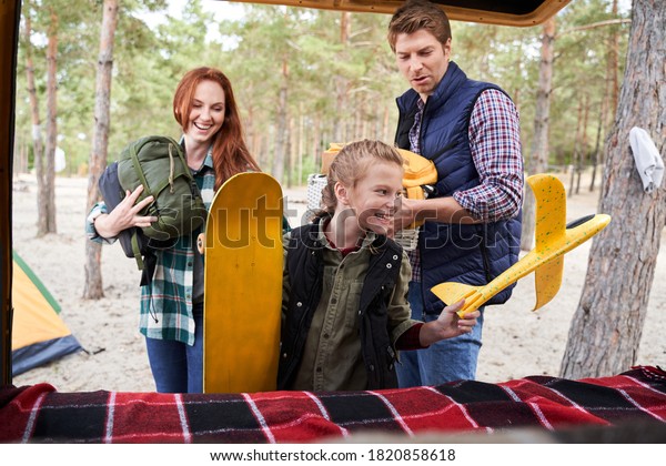 My best family. Delighted girl can\'t wait to\
play with her yellow toy airplane. Parents hold picnic items and\
admire their cute daughter