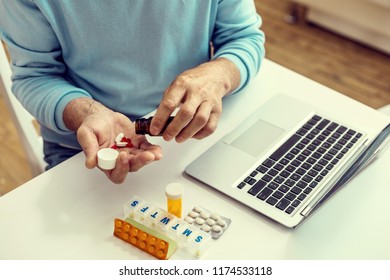 My daily dose. Top view on a hand of a retired gentleman sitting at a table and taking his medication. - Shutterstock ID 1174533118