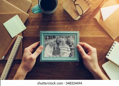My family is my inspiration. Close-up top view of man holding photograph of his family over wooden desk with different chancellery stuff laying around