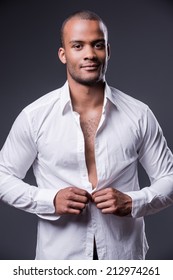 It Is My Favorite Shirt. Handsome Young Black Man Dressing Up His Shirt And Smiling While Standing Against Grey Background