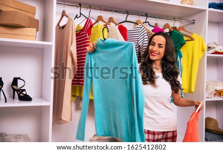 My favorite sweatshirt. Close-up photo of a happy girl in pajamas, who is holding two colorful items of clothing, choosing which one to wear.