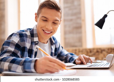My favourite subject. Handsome smiling fair-haired boy working on his laptop and writing in his notebook while sitting at the table
