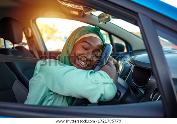 My First Car.\
Visiting car dealership. Beautiful woman is hugging her new car and\
smiling. Young and cheerful woman enjoying new car hugging steering\
wheel sitting inside.