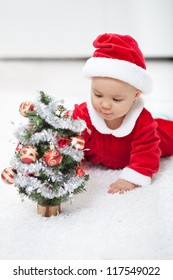 My First Christmas - Baby Girl In Santa Outfit With Small Decorated Tree