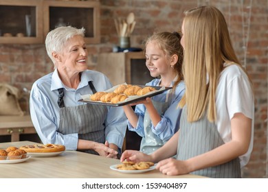 My First Homemade Pastry. Joyful Girl Holding Tray And Smelling Freshly Baked Croissants, Cooking With Mom And Granny, Kitchen Interior