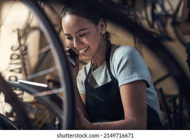 My hobby is my keepsake. Shot of a young happy young woman talking on a cellphone and using a digital tablet while fixing a bike at a bicycle repair shop. - Powered by Shutterstock