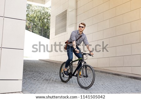 My lifestyle. Positive handsome man smiling while riding on his bike to work