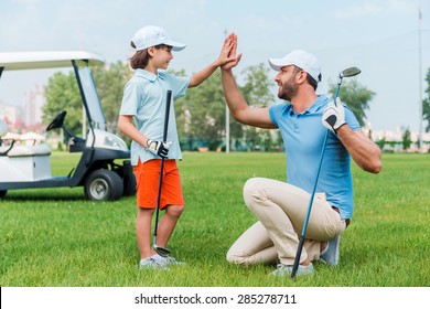 My little winner! Cheerful young man and his son giving high-five to each other while standing on the golf course