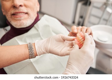 Its my new teeth. Cropped view of the dentist showing to senior grey haired patient teeth dentures while working at the dental clinic. Man sharing satisfaction smile