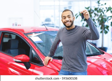 My New Wheels. Attractive Young African Man Smiling Happily Holding Car Keys To His Newly Bought Car Posing At The Dealership Copyspace Driver Owner Purchase Consumerism Happiness Buying A Car Concept