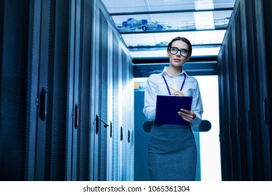 My report. Inspired serious woman taking notes and standing new server cabinets
