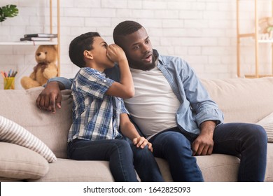 My secret. Little Afro Boy Whispering In Father's Ear, sharing secret while sitting together on coiu