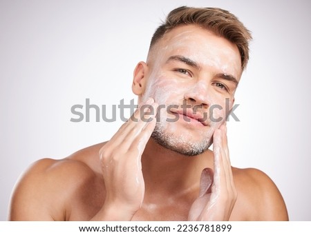 My skin loves this product. Studio shot of a young man washing his face against a grey background.
