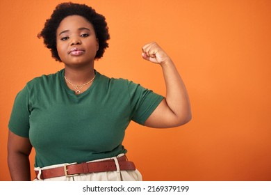 My Strength Comes From Within. Shot Of A Beautiful Young Woman Flexing While Standing Against An Orange Background.