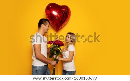 You’re my Valentine. A man is presenting a big red heart-shaped balloon and a bouquet of roses to his significant other, while she is giving him a radiant smile in return.