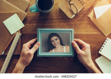 My Wife Is My Inspiration. Close-up Top View Of Man Holding Photograph Of Beautiful Young Woman Over Wooden Desk With Different Chancellery Stuff Laying Around