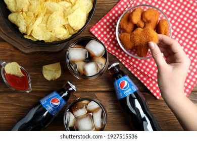 MYKOLAIV, UKRAINE - FEBRUARY 16, 2021: Woman Eating Chicken Nuggets At Wooden Table With Pepsi, Top View